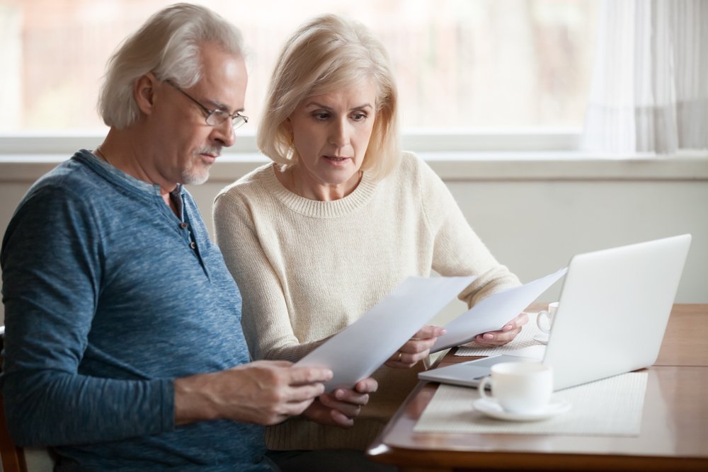 A senior couple sitting at a table, reviewing documents and discussing estate planning to ensure their wishes are met and their family is provided for in the future.