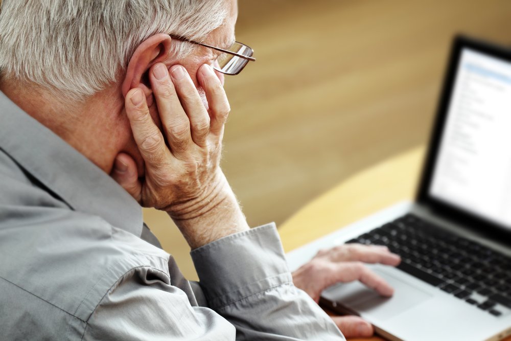 A senior man sitting at a desk using a computer, exploring information about electronic wills and their impact on estate planning and elder law.
