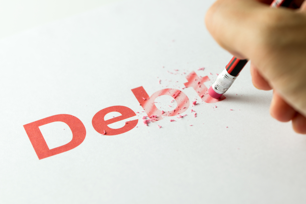 A red pencil erasing the word "debt" on a piece of paper, symbolizing strategies to manage and eliminate debt before retirement in the context of estate planning and elder law.