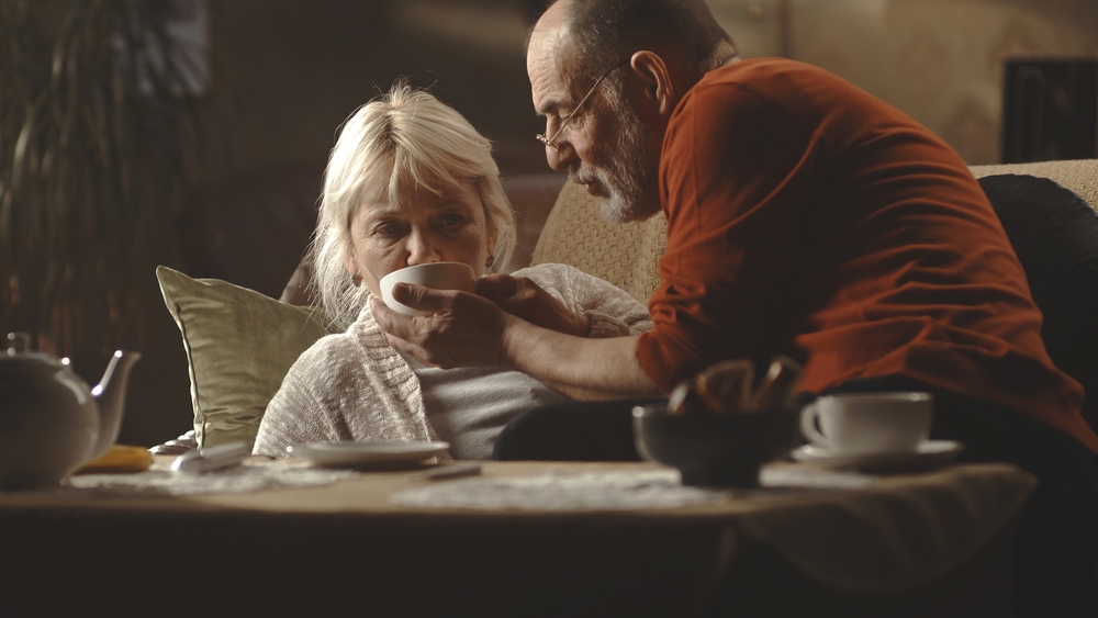 An elderly husband offering a cup of tea to his sick wife, highlighting the importance of care and support in guardianship, relevant to estate planning and elder law themes.