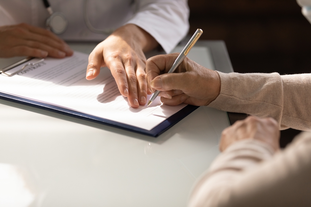 A person signing legal documents at a desk, symbolizing the complexities of elder law and estate planning in nursing home admissions.