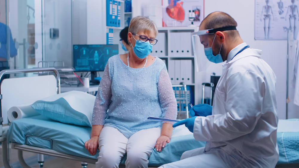 Senior woman wearing a mask discussing with a doctor and signing a health care proxy form at a hospital, highlighting the importance of personalized estate planning and elder law considerations.