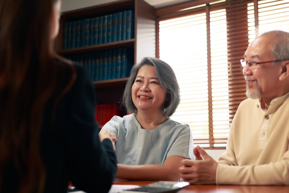 An Asian senior couple converses with a professional advisor about Medicaid planning, highlighting the need for expert consultation in estate planning and elder law.