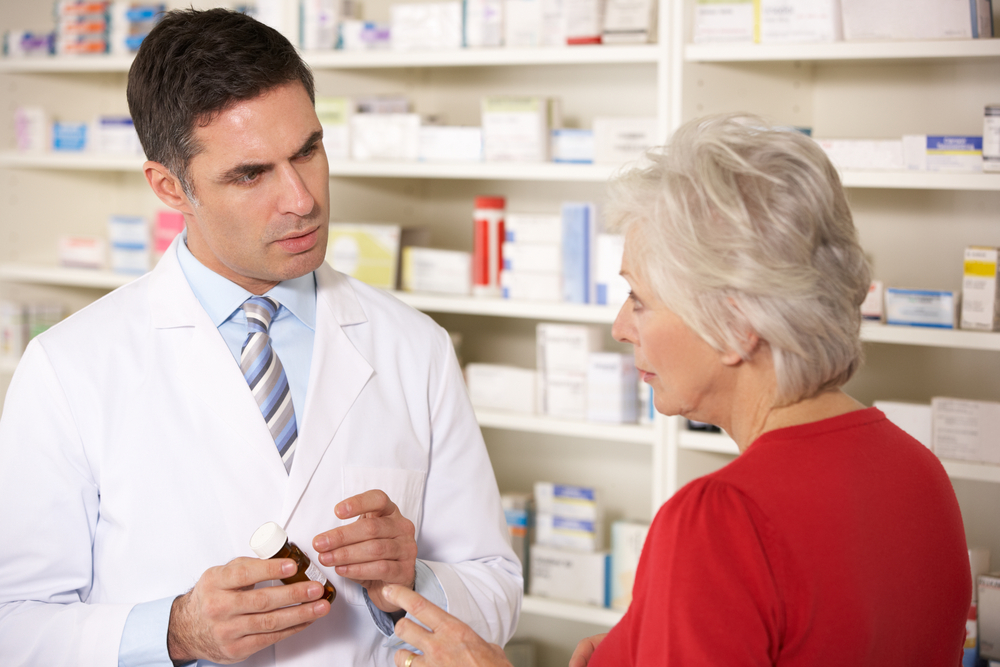 Senior woman talking with a pharmacist in a pharmacy, discussing possible Medicare plan changes and options during the Annual Notice of Change period.