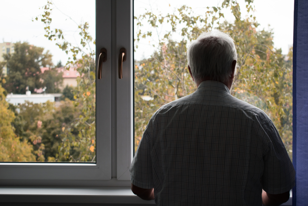 An elderly man stands alone in a dimly lit room, representing the challenges faced by middle-income seniors who are caught between Medicaid thresholds and financial security, emphasizing the need for thoughtful estate planning and elder law considerations.