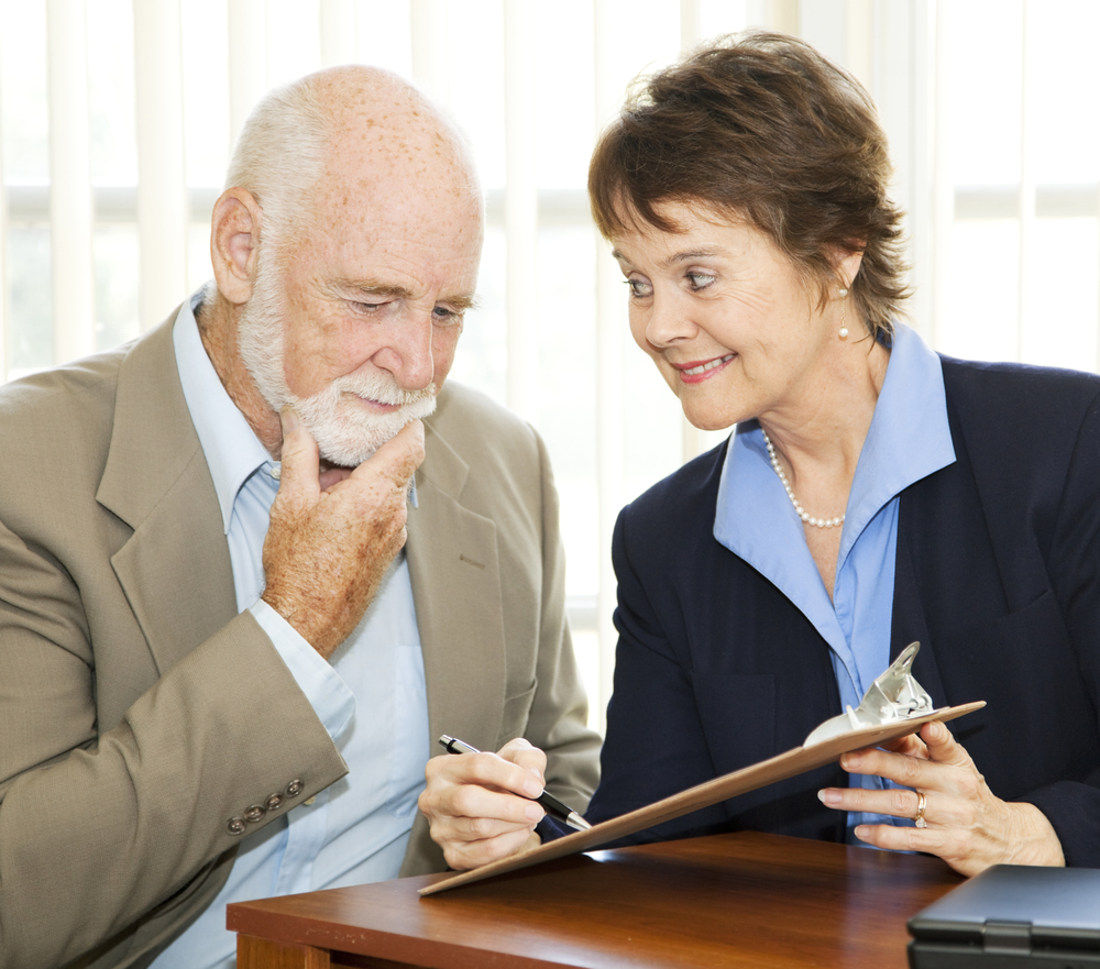Elderly man attentively examines a contract from a businesswoman, symbolizing the importance of informed decision-making in Medicare Advantage plan enrollment amidst aggressive marketing practices.