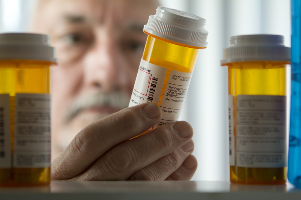 An elderly man carefully examines a prescription bottle, highlighting the challenges of understanding Medicare coverage in estate planning and elder law contexts.