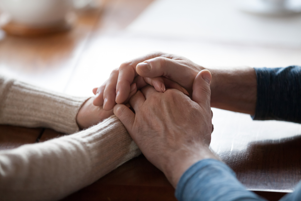 Close-up view of an elderly couple holding hands, symbolizing support and unity, relevant to Medicaid and estate planning for protecting spouses.