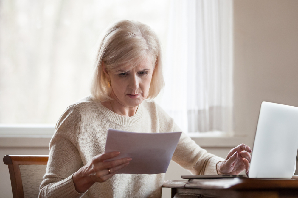An elderly woman appears confused as she reads through paperwork, symbolizing the complexities involved in understanding Medicaid and Medicare for elder law and estate planning.