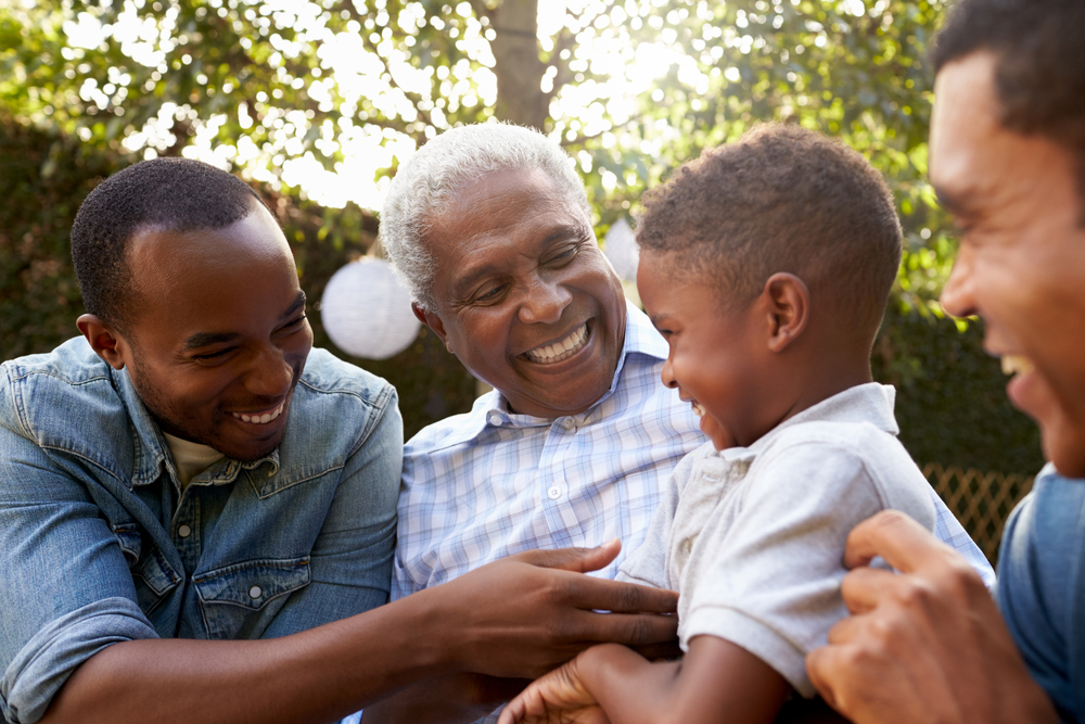 A happy multi-generational family, including a grandfather, sons, and grandson, smiling together in a garden, representing the importance of estate planning and having reliable power of attorney for managing family's future.