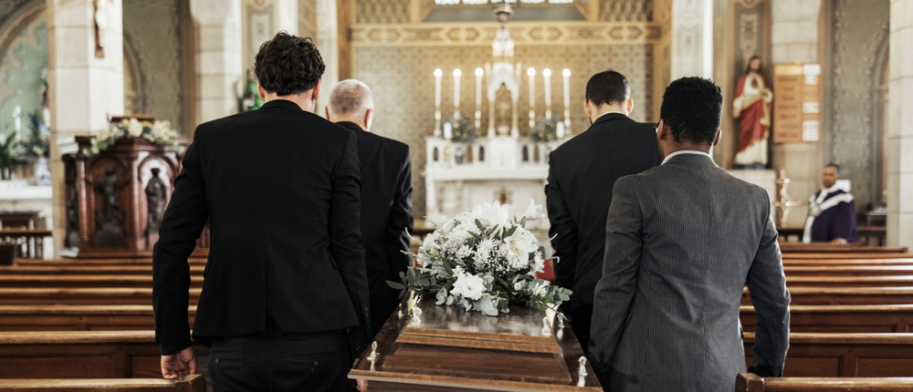 Pallbearers carry a coffin in a church, symbolizing the financial challenges of funeral planning and the potential assistance available through Medicaid benefits for families dealing with end-of-life expenses.
