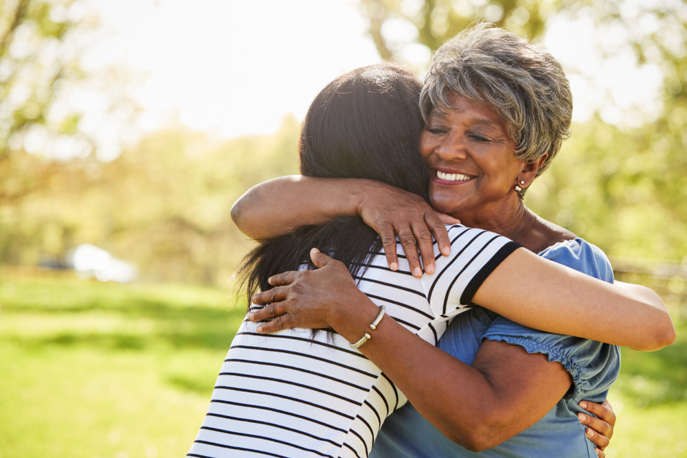 A senior mother and adult daughter hugging in a park, representing the decision-making process in estate planning related to naming beneficiaries and legacy planning.