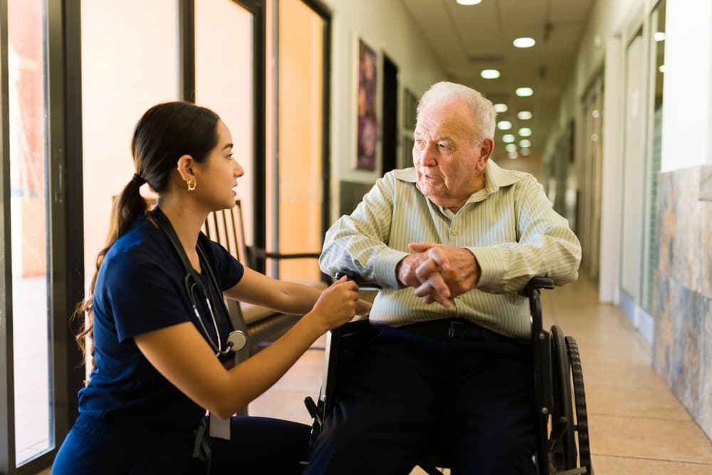 A nurse providing comfort to an elderly man in a wheelchair, illustrating the kind of compassionate care found in both nursing homes and hospice settings, focusing on the differences in care strategies.
