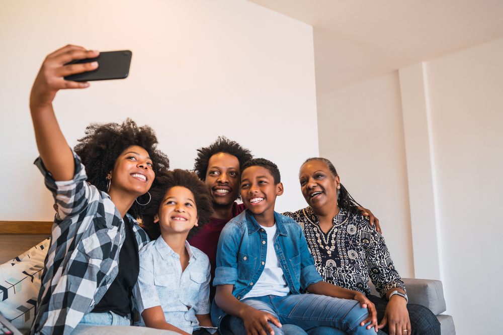 A joyful multigenerational African American family taking a selfie in their home, symbolizing the importance of designating beneficiaries in estate planning to protect family interests and avoid disputes.
