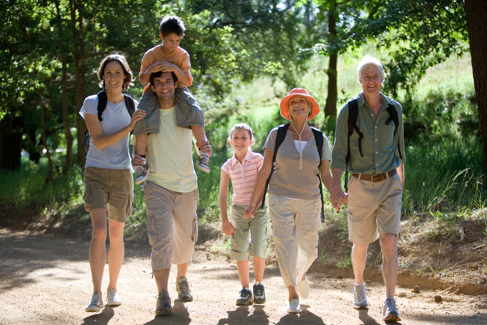 Multigenerational family with a young boy on his father's shoulders hiking on a mountain trail, illustrating the importance of estate planning and elder law in managing and protecting family inheritances.
