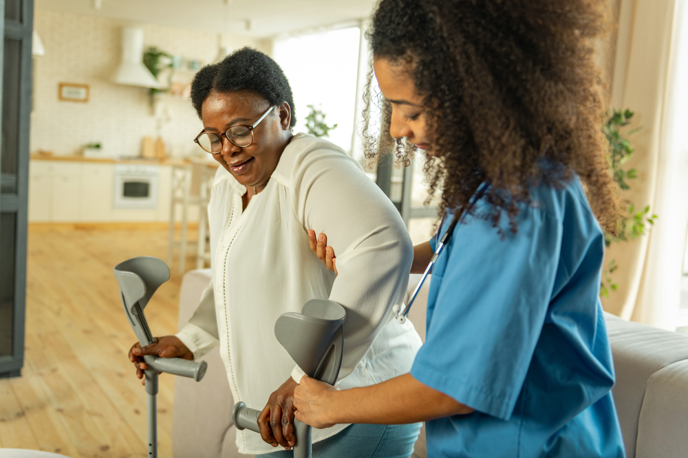 A nurse holding crutches helps an elderly patient at home, illustrating the importance of home health care services in elder law and estate planning discussions.
