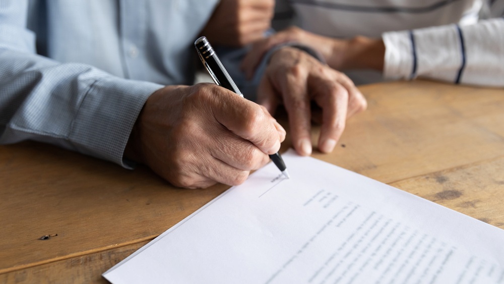 Senior man signing legal documents with a notary, emphasizing the critical role of proper notarization in estate planning for individuals diagnosed with dementia.