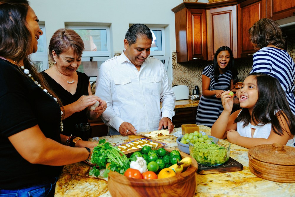Multigenerational family, including grandparents, parents, and children, joyfully preparing appetizers together in a cozy kitchen, representing the sandwich generation managing family care across generations.