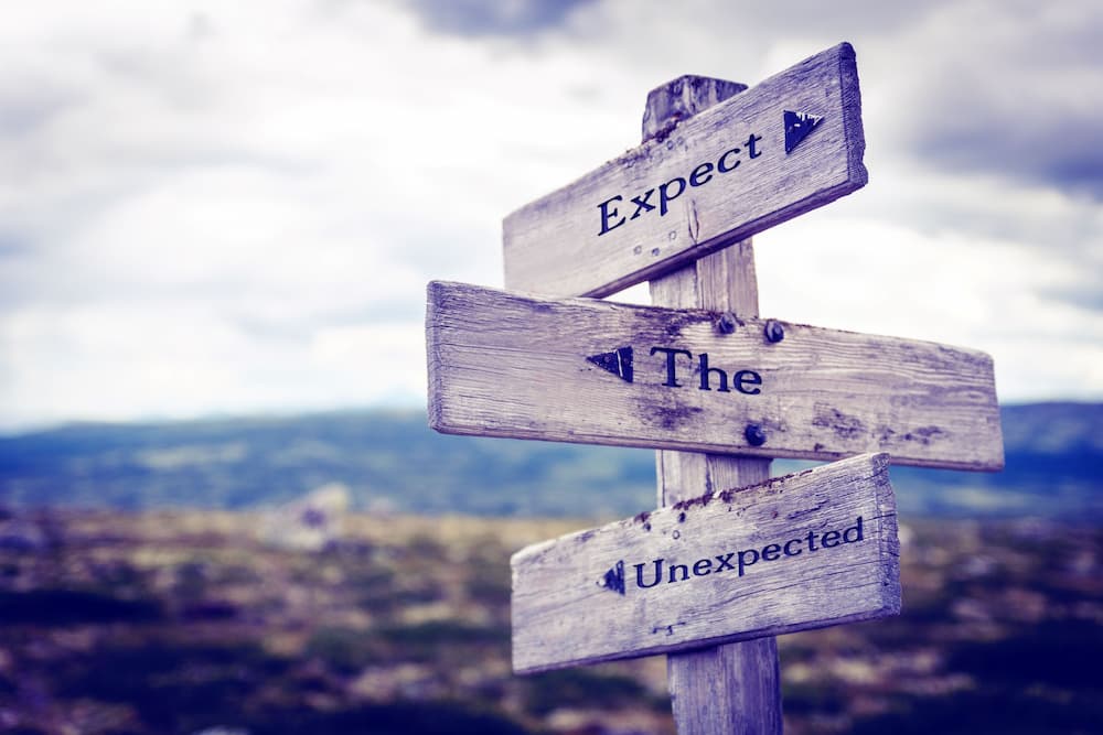 Wooden signpost outdoors with "Expect the Unexpected" written on it, symbolizing the importance of planning for future healthcare decisions with a living will in estate planning and elder law contexts.