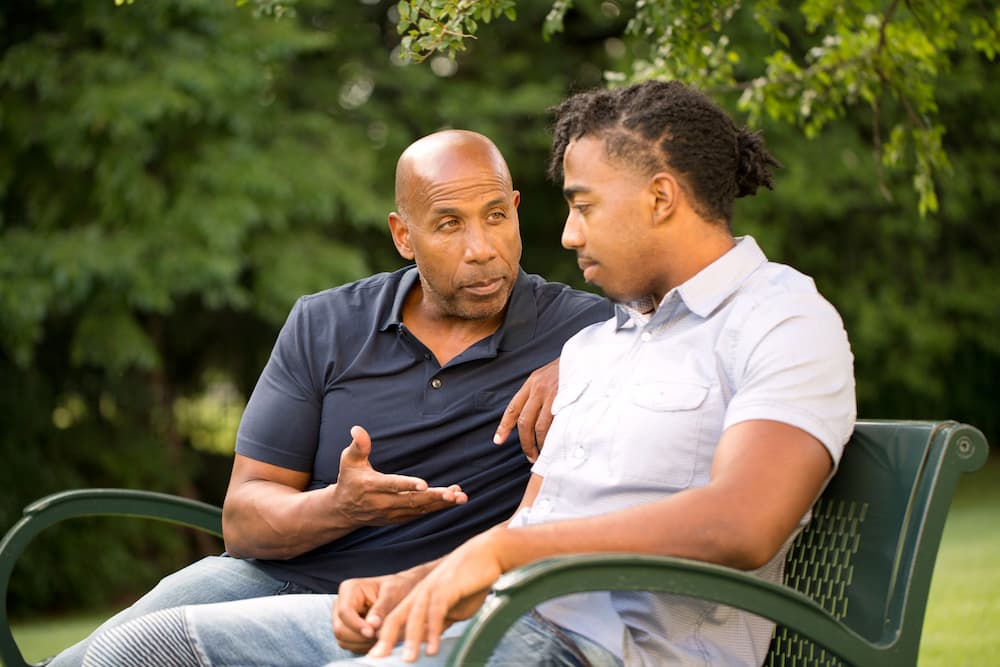 Middle-aged man having a conversation with his adult son on a park bench, symbolizing discussions on equitable asset distribution in estate planning and elder law.