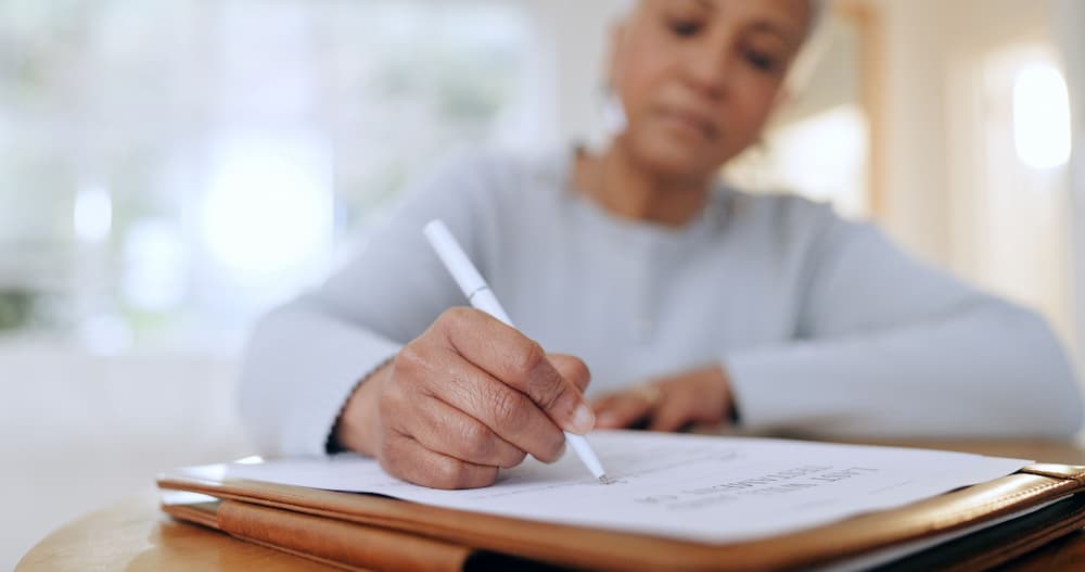 Senior woman signing her last will and testament at a desk, emphasizing the need for estate planning and will creation for all individuals.