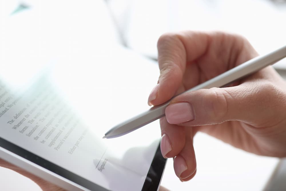 A woman's hand using a stylus to sign an estate planning document on a tablet, illustrating secure digital document management in estate planning and elder law.