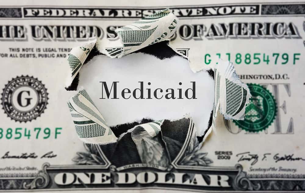 A ripped dollar bill revealing the word Medicaid, symbolizing the financial aspect of Medicaid coverage in the context of estate planning and elder law.