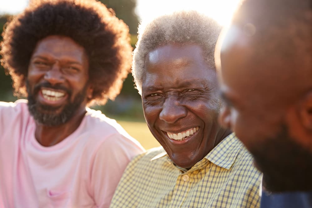 A senior man with his two adult sons, laughing and talking outdoors, symbolizing the conversation about estate planning, inheritance, and designating contingent beneficiaries in the family estate plan.