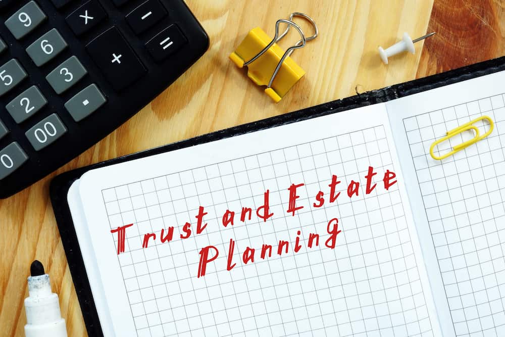 The words "Trust and Estate Planning" handwritten on a sheet of paper, emphasizing the critical role of trusts in estate planning for efficient asset management and legal arrangements.
