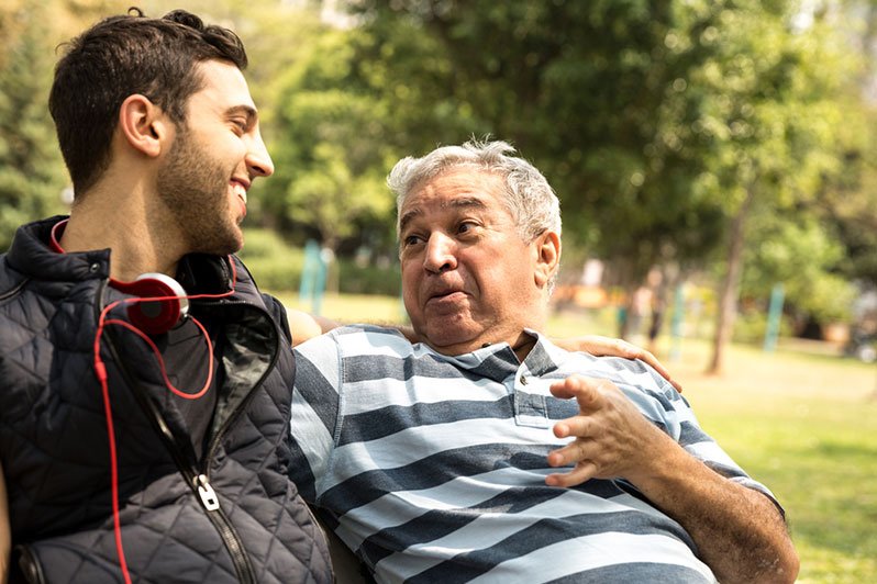 An older man and his adult son sitting together on a park bench, engaged in a serious conversation, representing the importance of choosing a reliable agent for estate and incapacity planning.