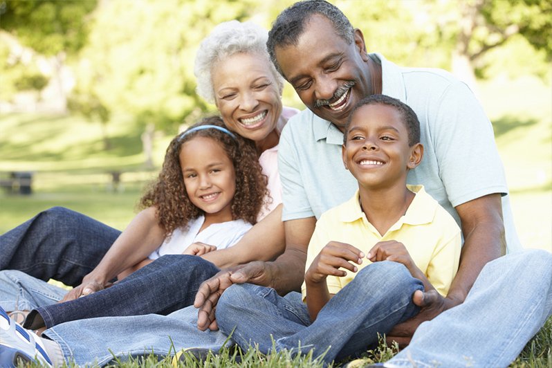 An elderly couple enjoying a moment with their young grandchildren while planning their estate, highlighting the importance of including grandchildren in a will and considering age stipulations and trusts.