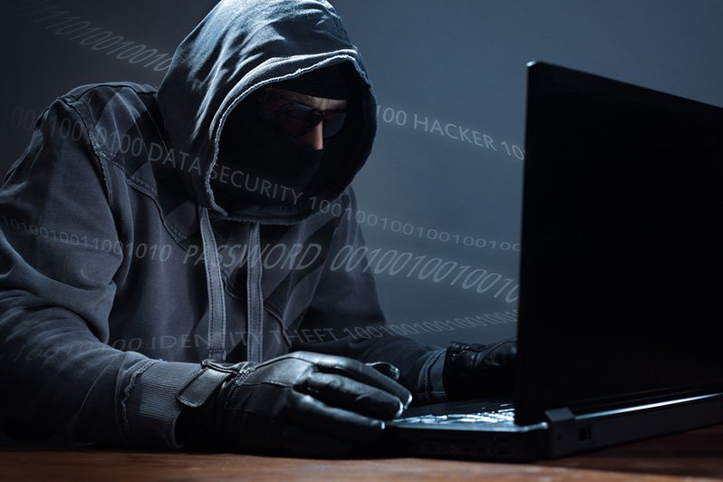 A dark, shadowy figure at a computer, symbolizing the threat of identity theft targeting deceased individuals, highlighting the importance of estate planning and elder law to protect personal information.