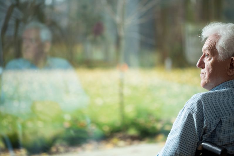 An elderly woman sitting at a window, gazing outside with a contemplative expression, illustrating the theme of loneliness and the potential relief through estate planning strategies that improve social connections for seniors.