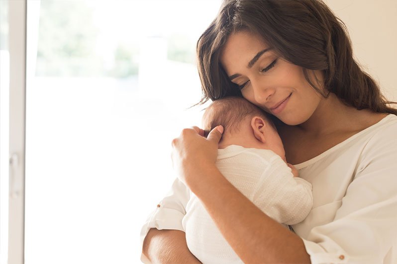 A new mother holding her baby, emphasizing the significance of estate planning and wills in protecting her child's future.