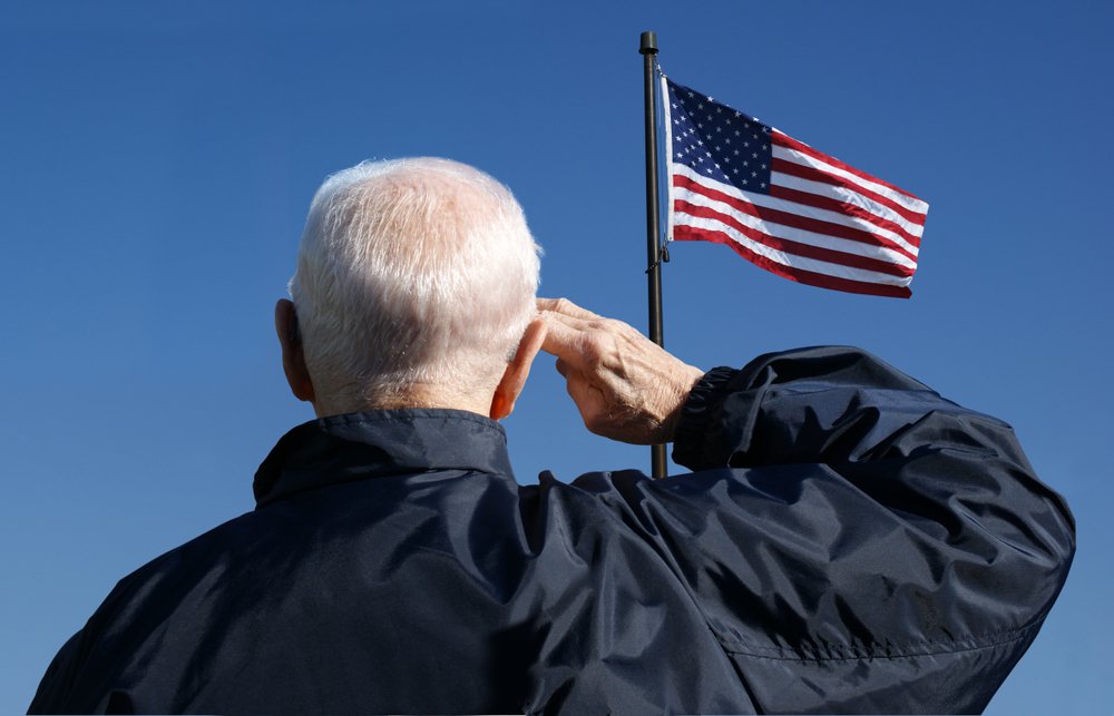 An elderly couple discussing estate planning and Veterans Pension benefits with a legal advisor, emphasizing changes in eligibility due to new net worth regulations.