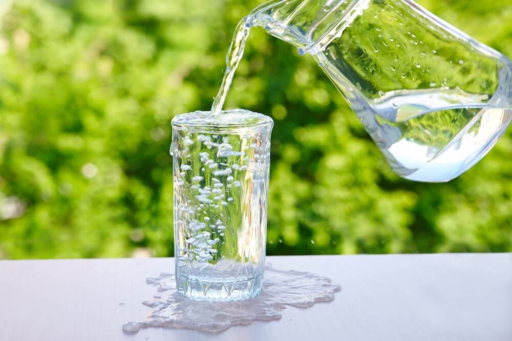 A clear pitcher pours water into a glass, causing it to overflow against a vibrant green background, illustrating how an estate can exceed tax limits if not carefully managed.