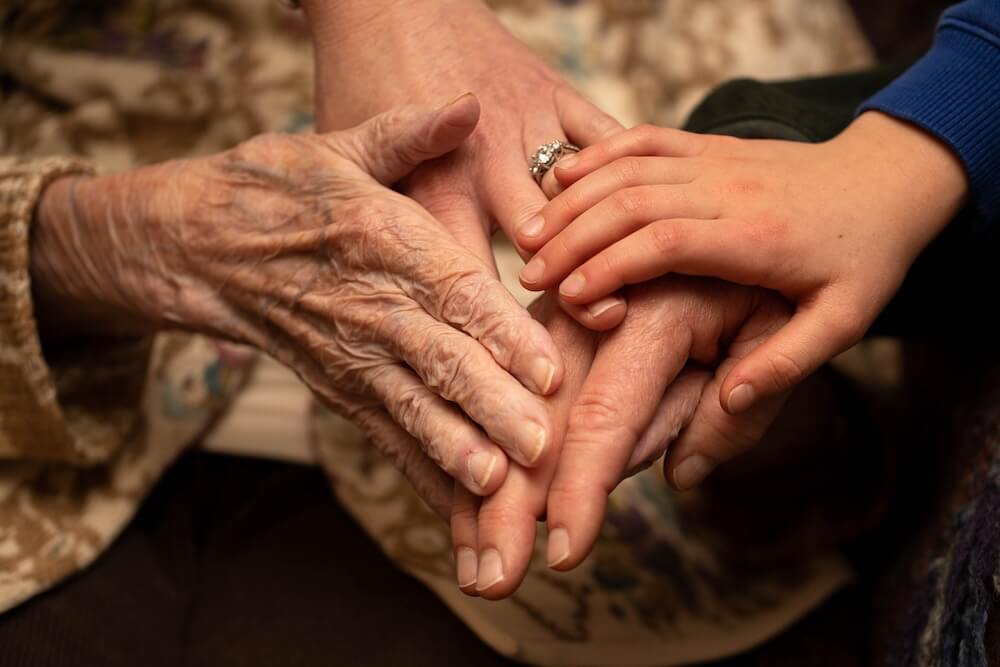 Close-up of an older adult’s hands joined by younger hands, reflecting the concept of multi-generational trust, unity, and wealth preservation.