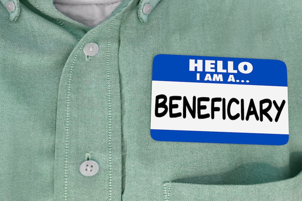 A close-up of a person wearing a green button-down shirt with a blue-and-white name tag that reads “Hello, I am a... Beneficiary.”