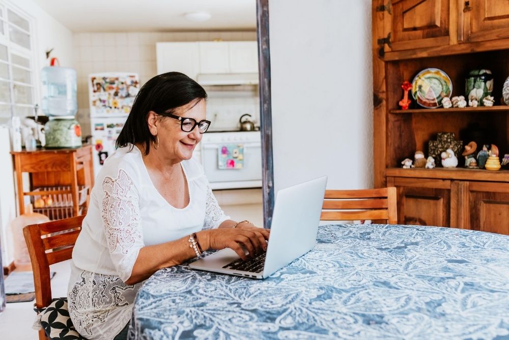 Older woman using a laptop at home while seated at a dining table