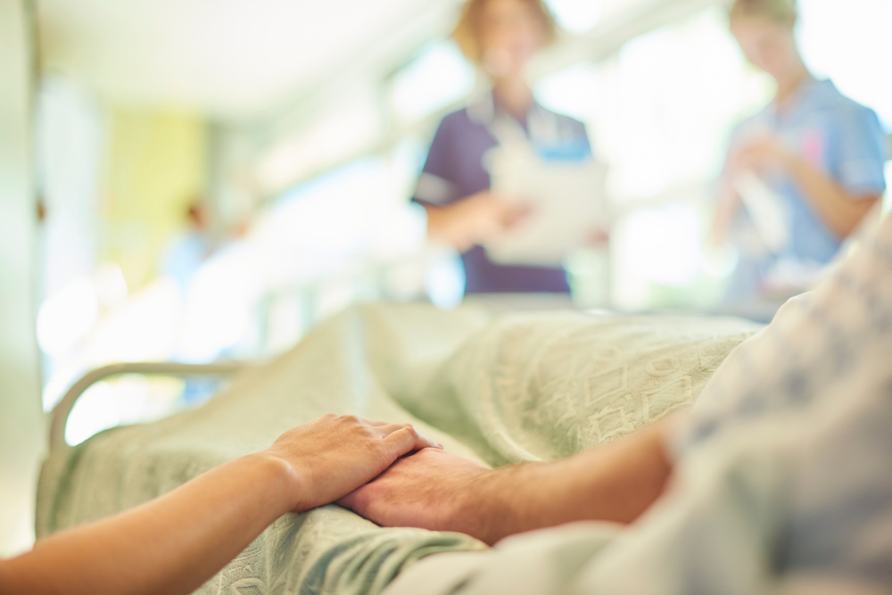 Patient in a hospital bed holding a loved one’s hand, illustrating the importance of medical directives and health care proxies during medical emergencies.