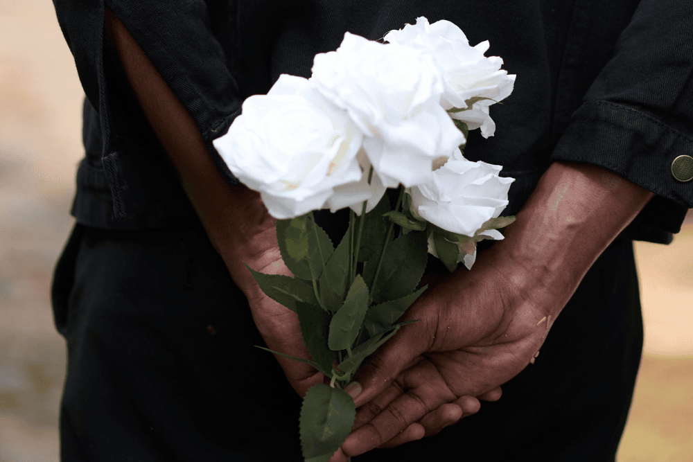 Hands holding white flowers at a funeral, representing funeral planning and the use of a funeral trust to cover burial expenses.