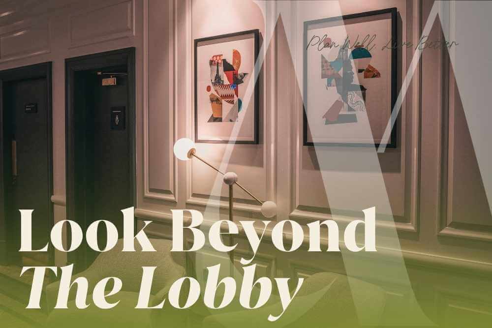 Hotel-style lobby hallway with framed art and a brass floor lamp, with the headline "Look Beyond the Lobby"